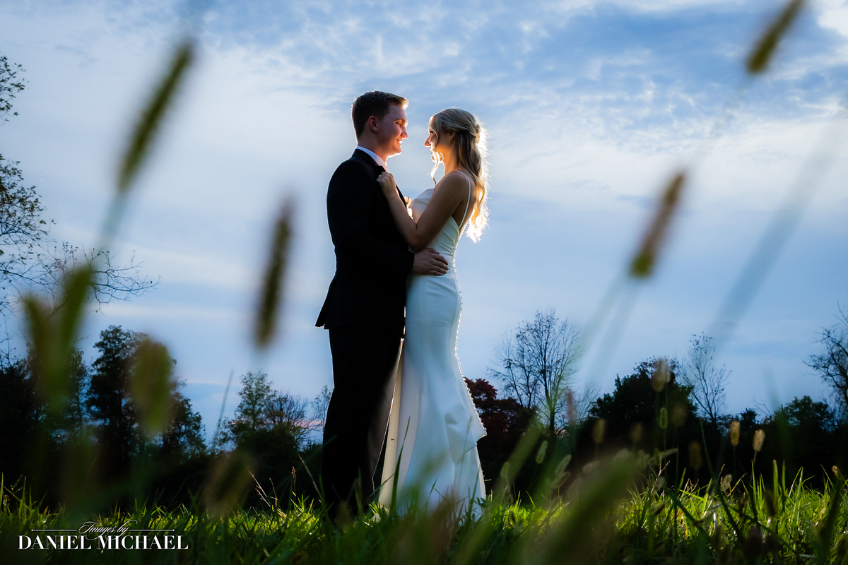a bride and groom embracing each other in a meadow with the sunlight shining on them